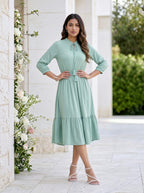 Woman in a light green dress standing in front of a decorative floral arrangement.