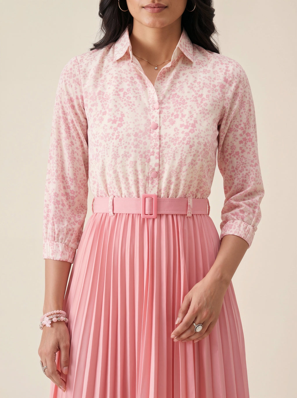 Woman wearing a pink floral blouse and pleated skirt against a beige background
