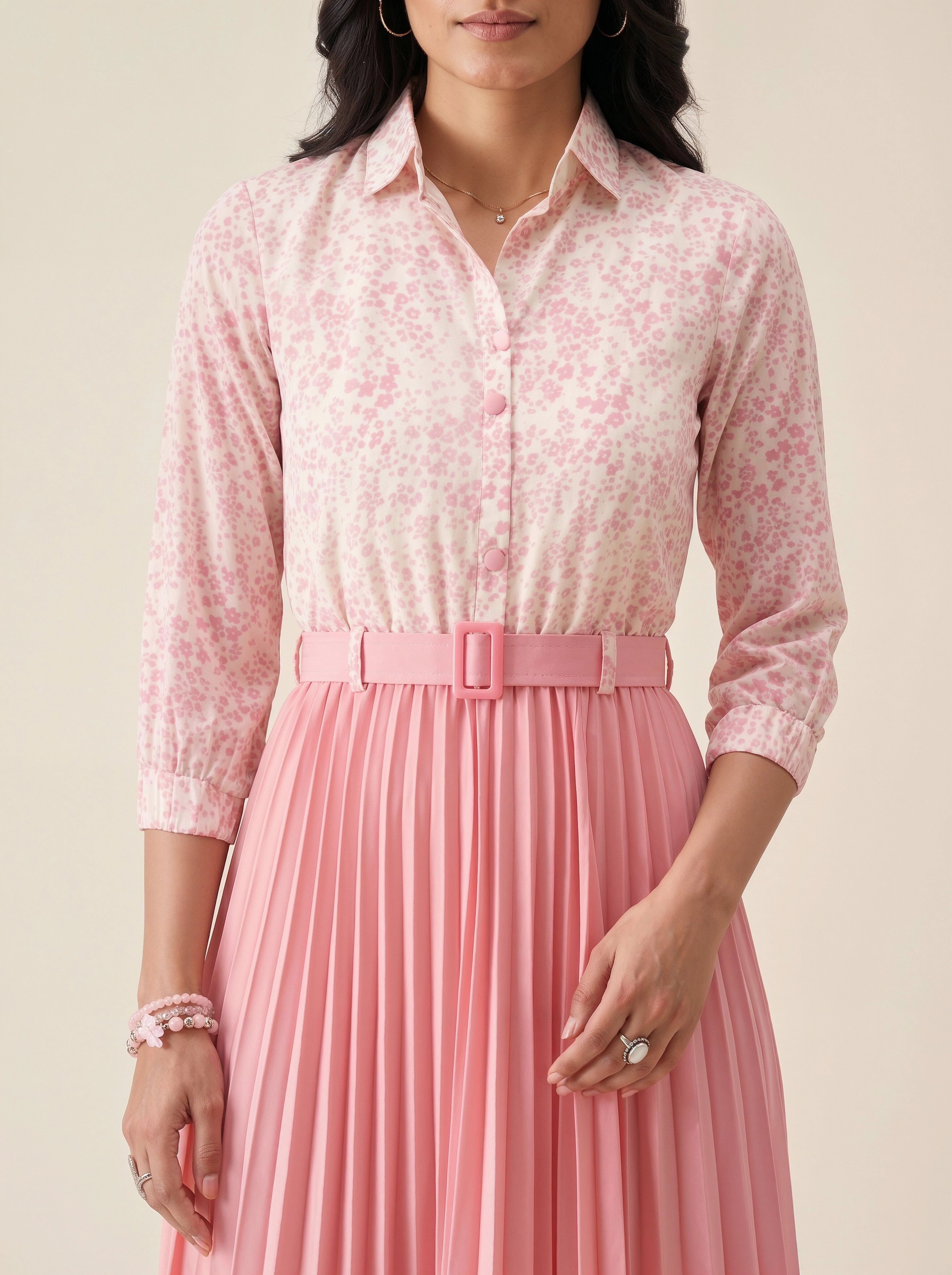 Woman wearing a pink floral blouse and pleated skirt against a beige background