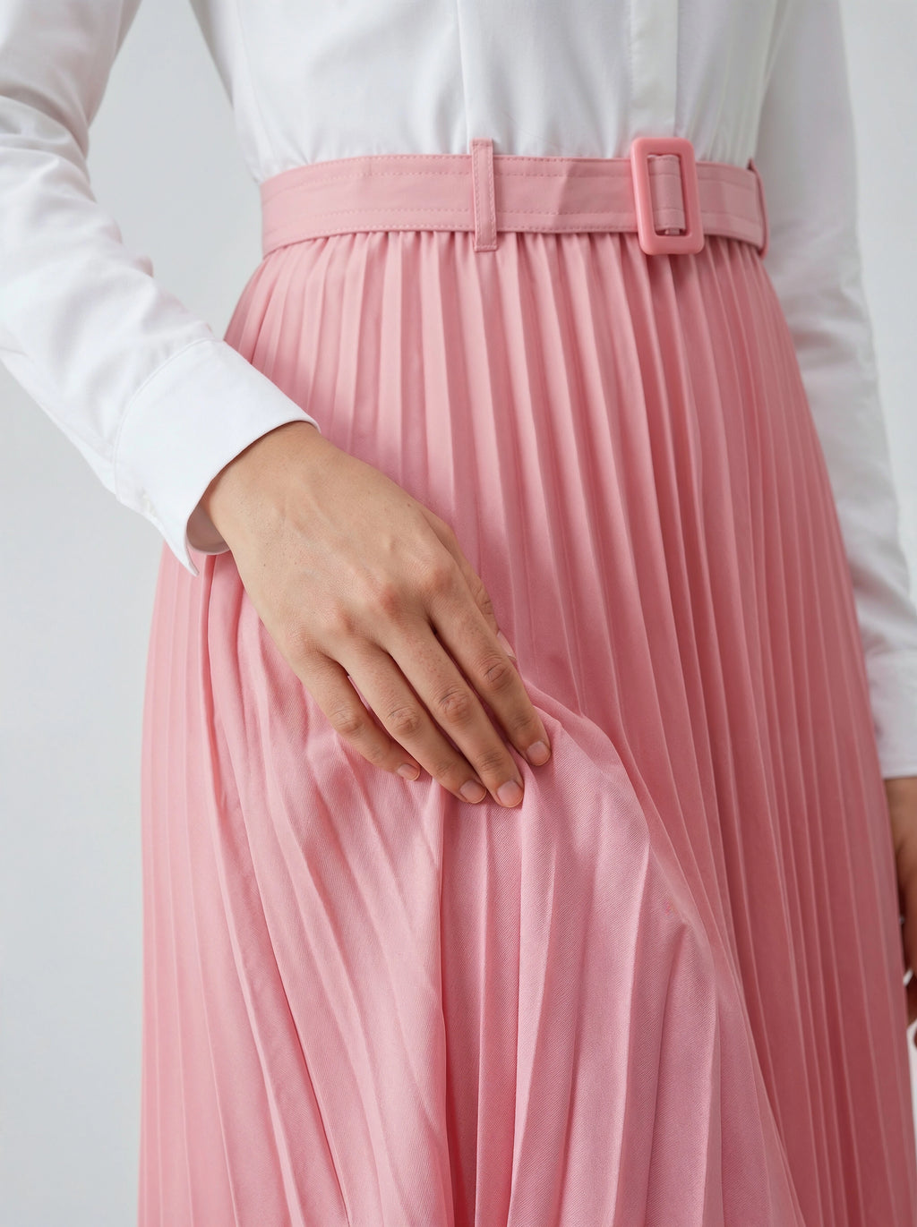 Person wearing a white shirt and pink pleated skirt with a belt on a light gray background