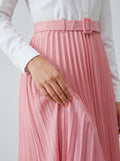 Person wearing a white shirt and pink pleated skirt with a belt on a light gray background