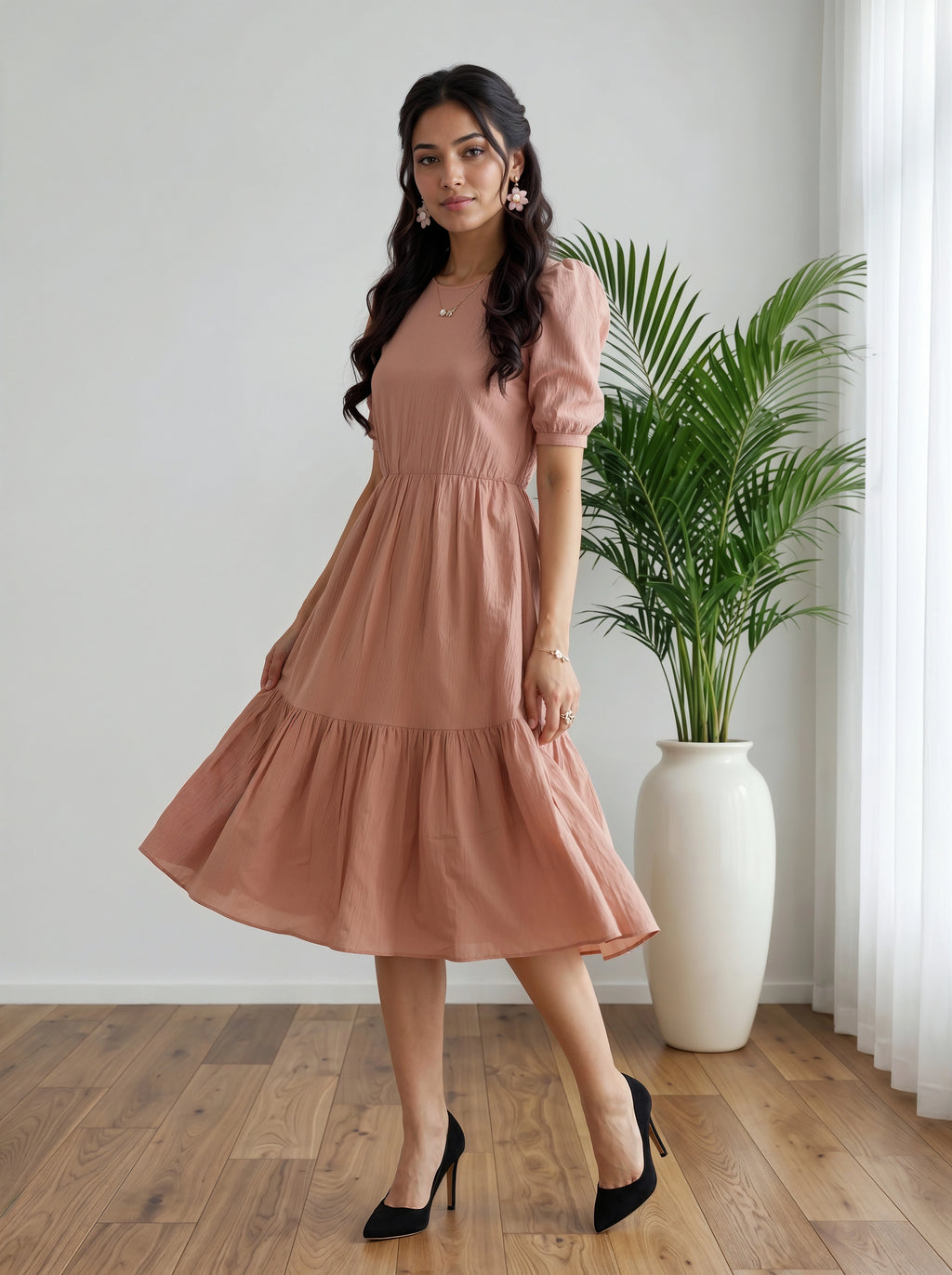 Woman in a pink dress standing in a room with a plant and white curtain.