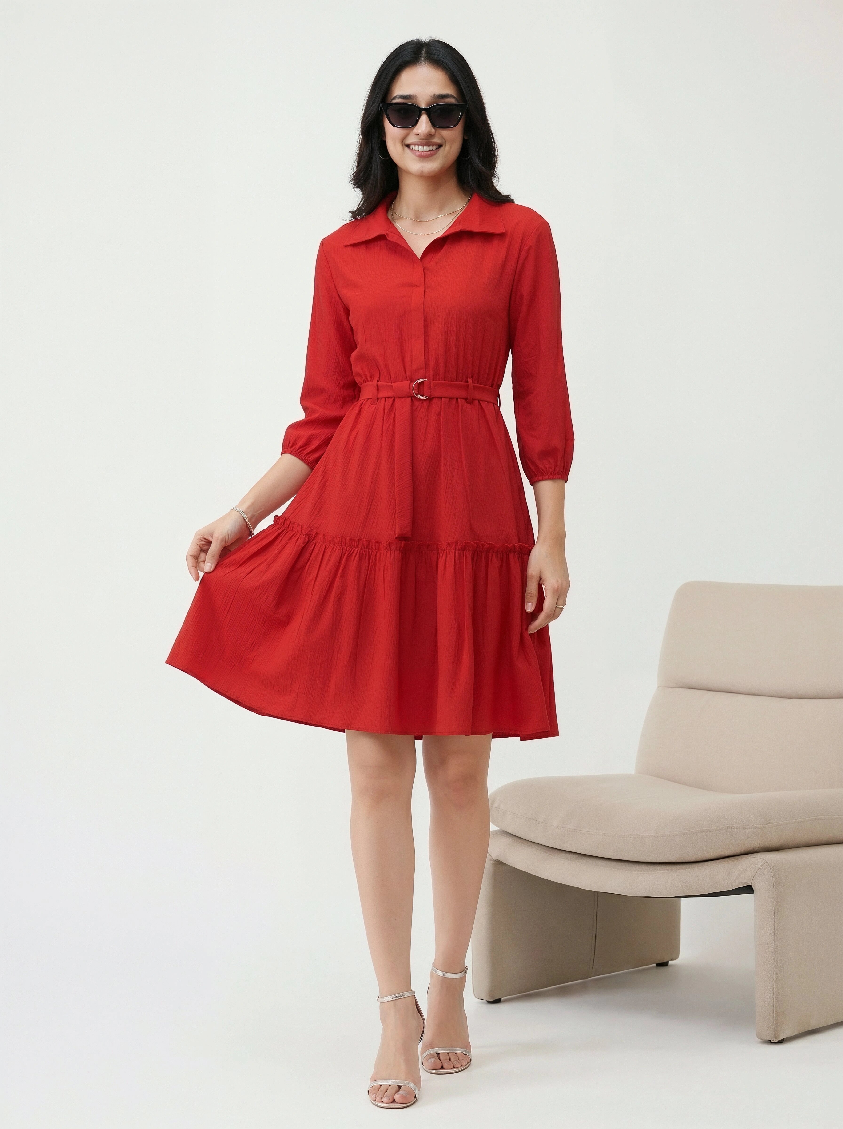 Woman wearing a red dress standing in a minimalistic room with a beige chair.