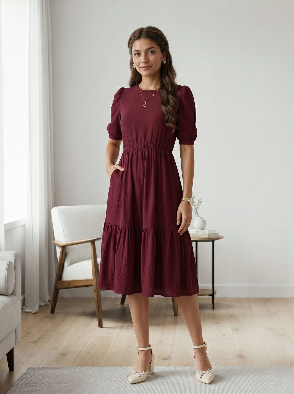 Woman in a burgundy dress standing in a room with light-colored walls and wooden flooring.