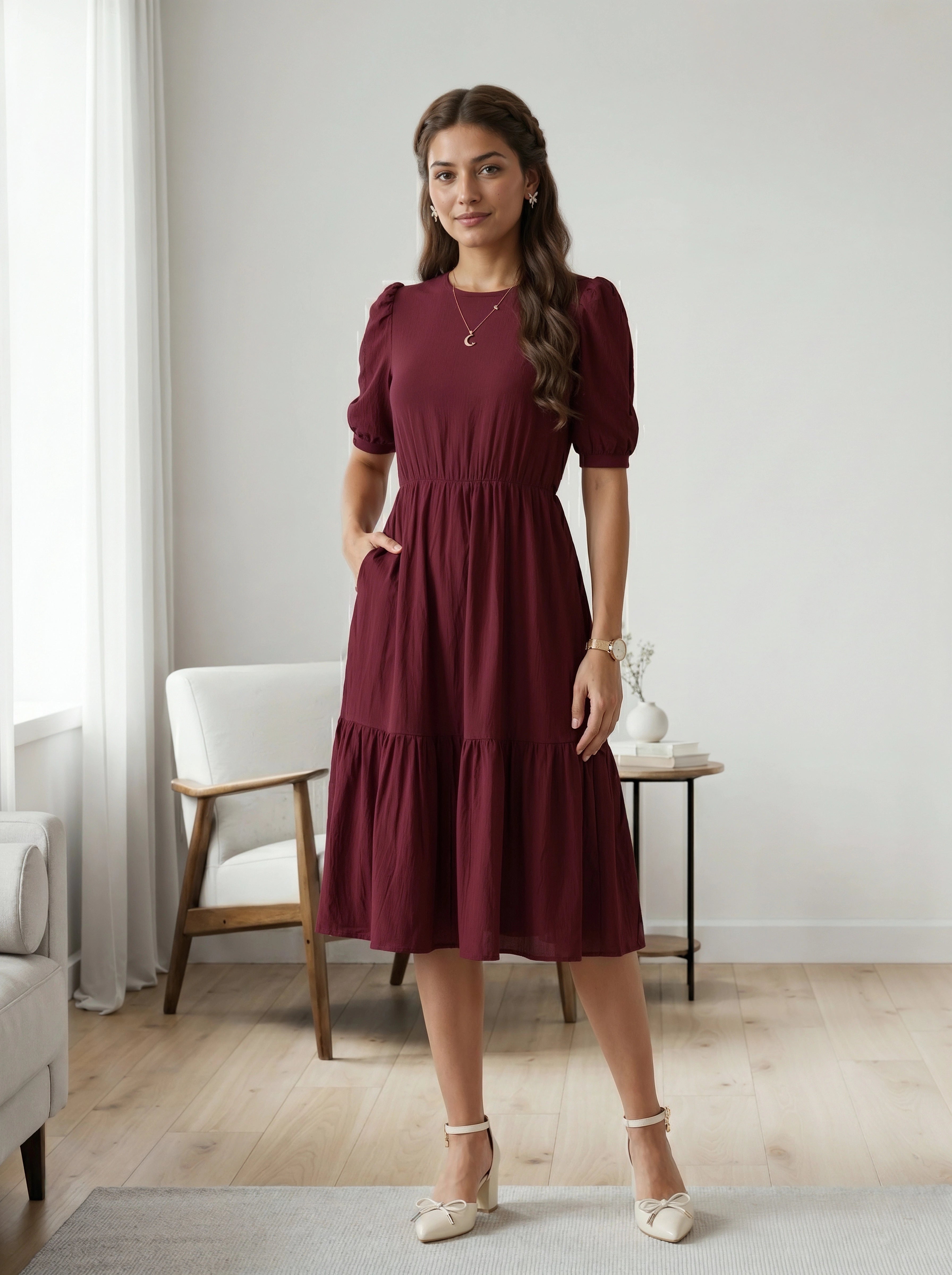 Woman in a burgundy dress standing in a room with light-colored walls and wooden flooring.