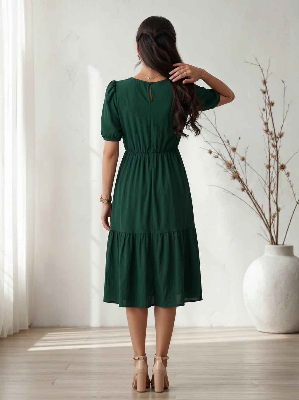 Woman wearing a green dress standing in a room with a white vase and plant.
