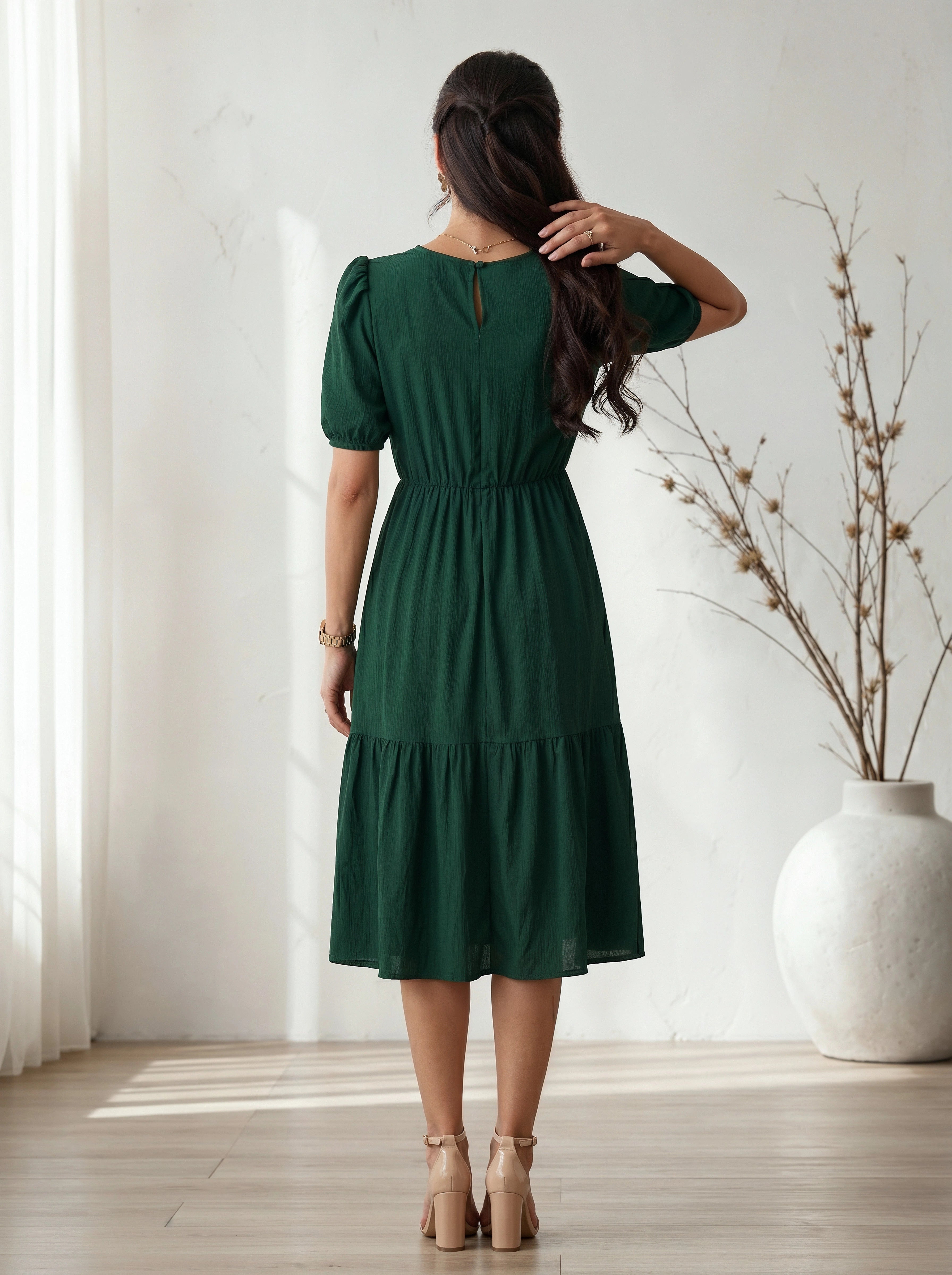 Woman wearing a green dress standing in a room with a white vase and plant.