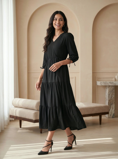 Woman wearing a black dress in an elegant room with beige walls and white curtains.