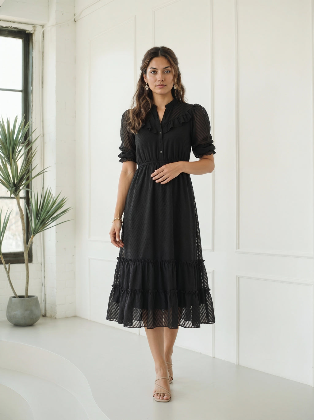 Woman wearing a black dress with long sleeves and a tiered skirt against a white wall.
