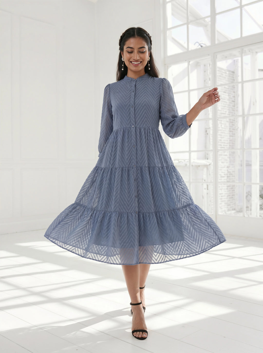 Woman wearing a blue dress standing in a bright room with large windows.