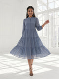 Woman wearing a blue dress standing in a bright room with large windows.