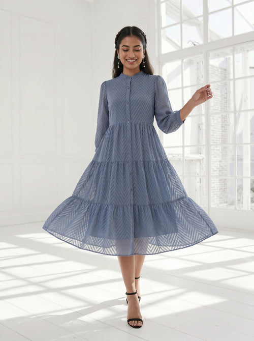 Woman wearing a blue dress standing in a bright room with large windows.