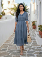 Woman in a blue dress standing on a stone path with plants and buildings in the background