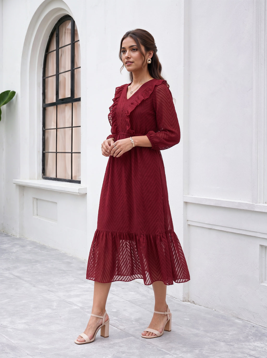 Woman wearing a red dress standing in front of a white wall with an arched window.