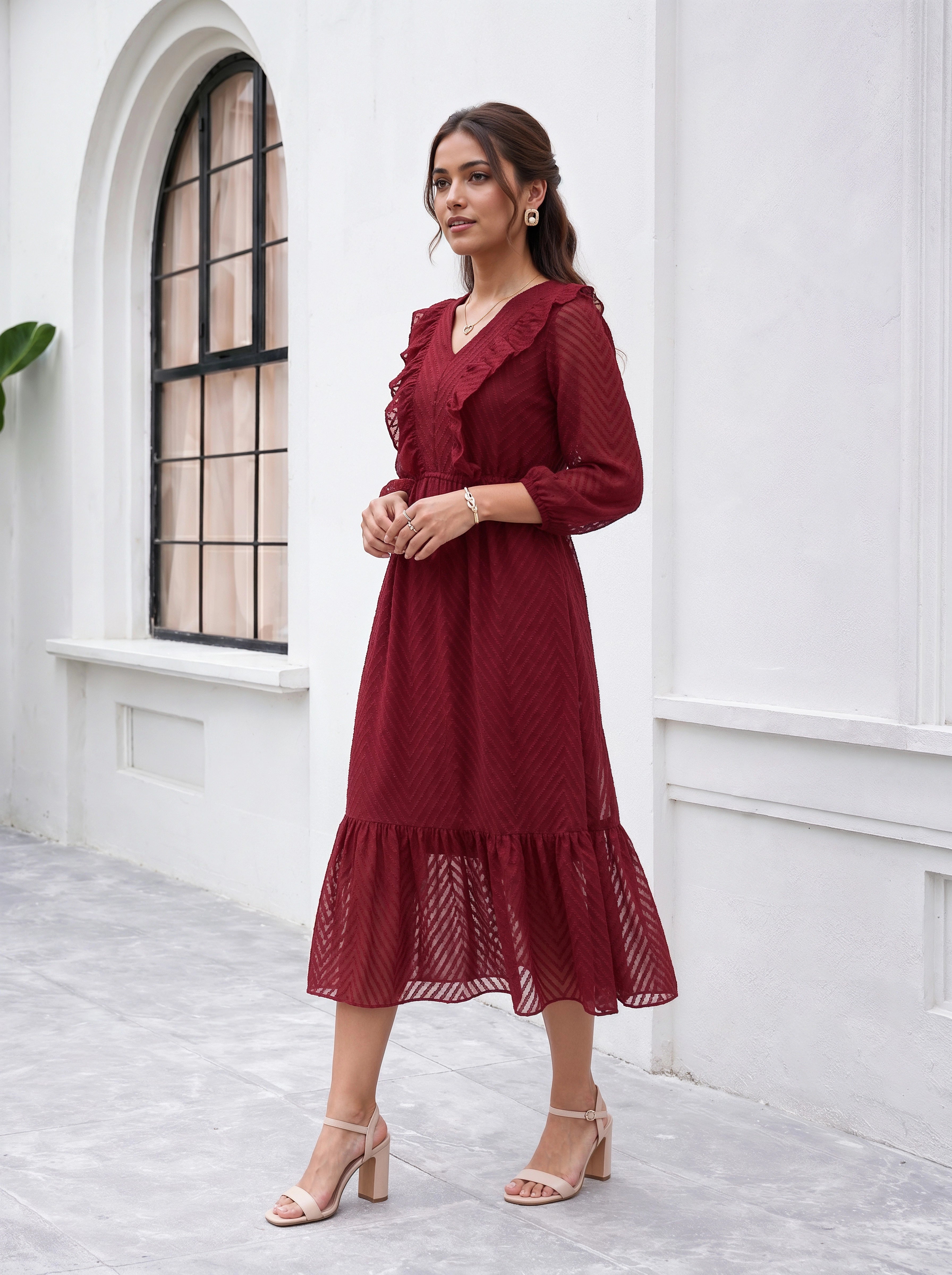 Woman wearing a red dress standing in front of a white wall with an arched window.