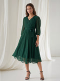 Woman wearing a green dress standing against a white curtain backdrop