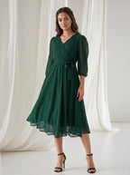 Woman wearing a green dress standing against a white curtain backdrop