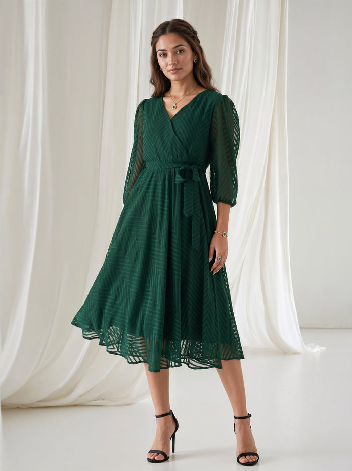 Woman wearing a green dress standing against a white curtain backdrop
