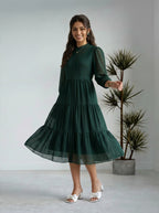 Woman wearing a green dress standing in a minimalistic room with a plant.