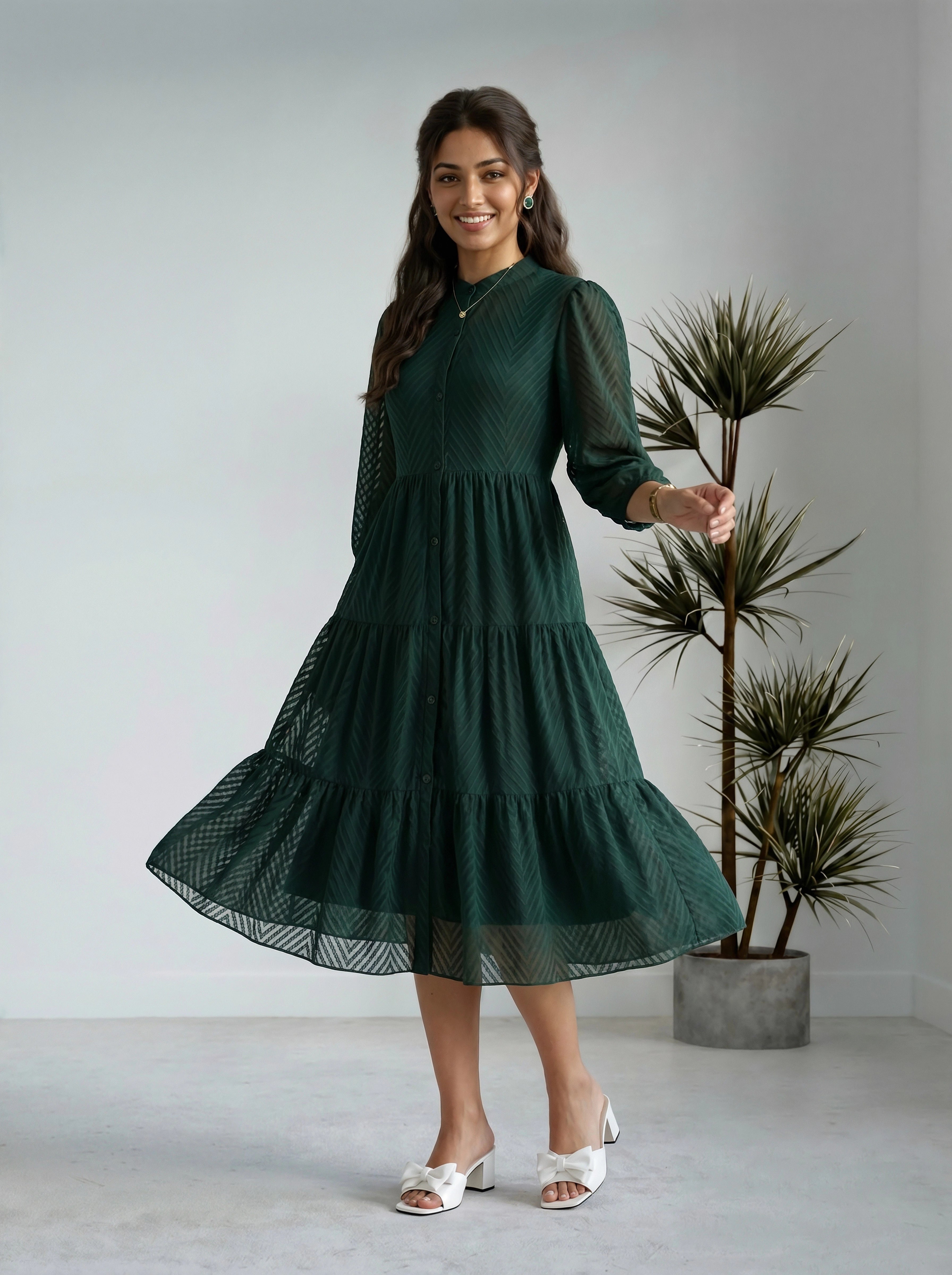 Woman wearing a green dress standing in a minimalistic room with a plant.