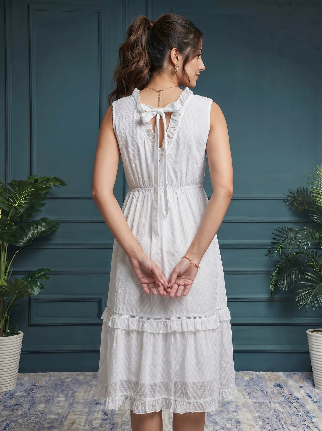 Woman wearing a white dress with a blue wall and plants in the background