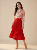 Woman wearing a red pleated skirt and floral blouse on a beige background
