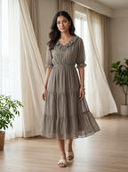 Woman wearing a gray dress standing in a room with curtains and plants.