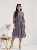 Woman wearing a gray patterned dress standing next to a small table with decor items on a white background
