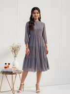 Woman wearing a gray patterned dress standing next to a small table with decor items on a white background