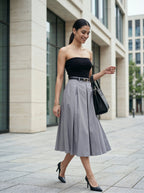 Woman in black strapless top and gray skirt walking on a city street.