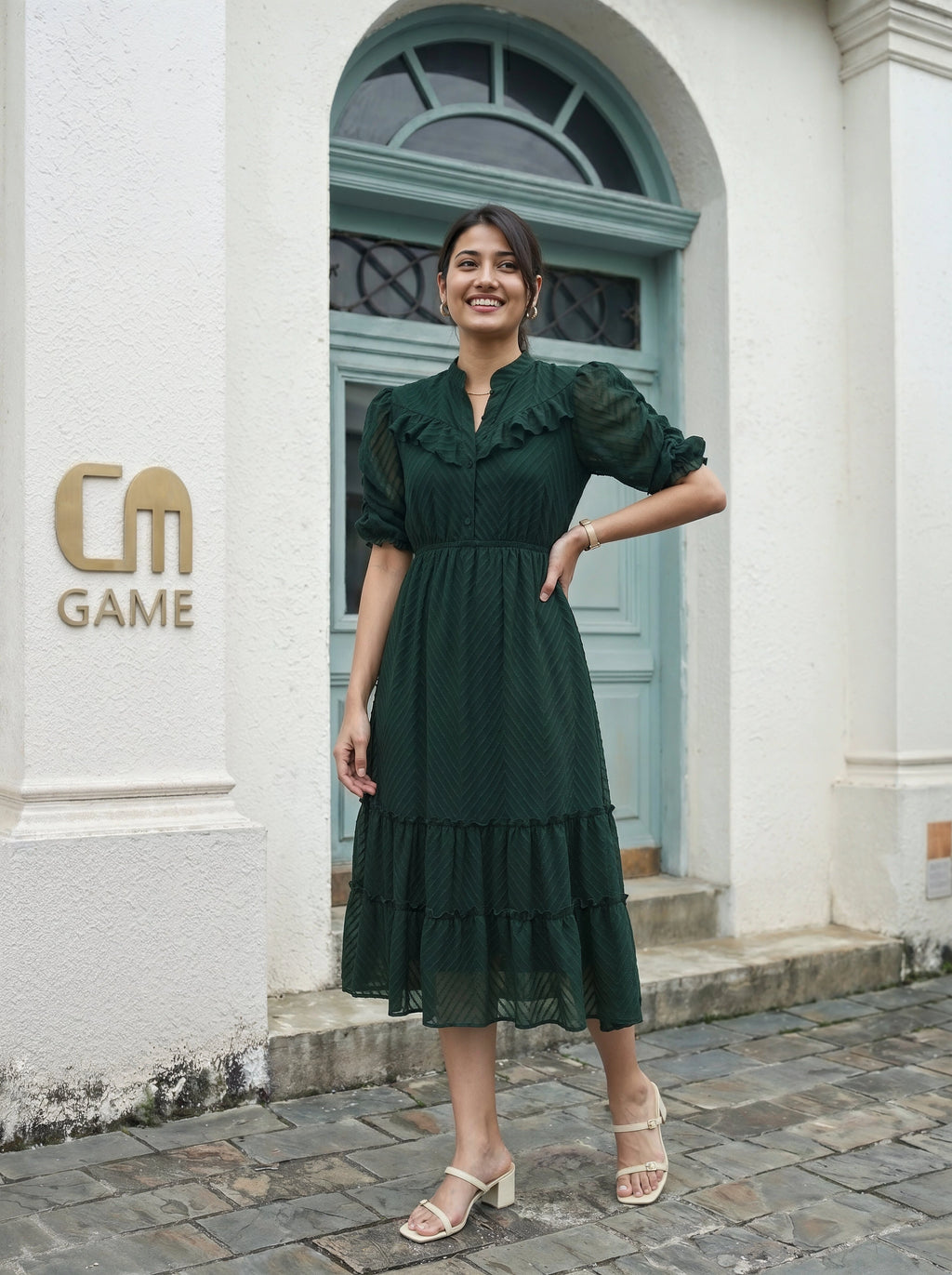 Woman in a green dress standing in front of a building with 'CM Game' logo.