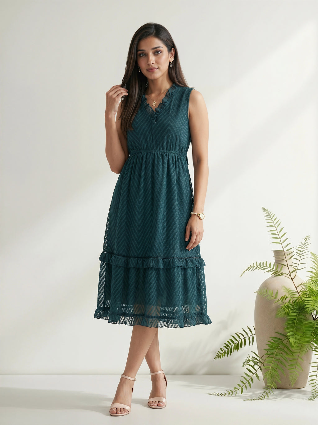 Woman wearing a teal dress standing against a white background with a plant to the side.