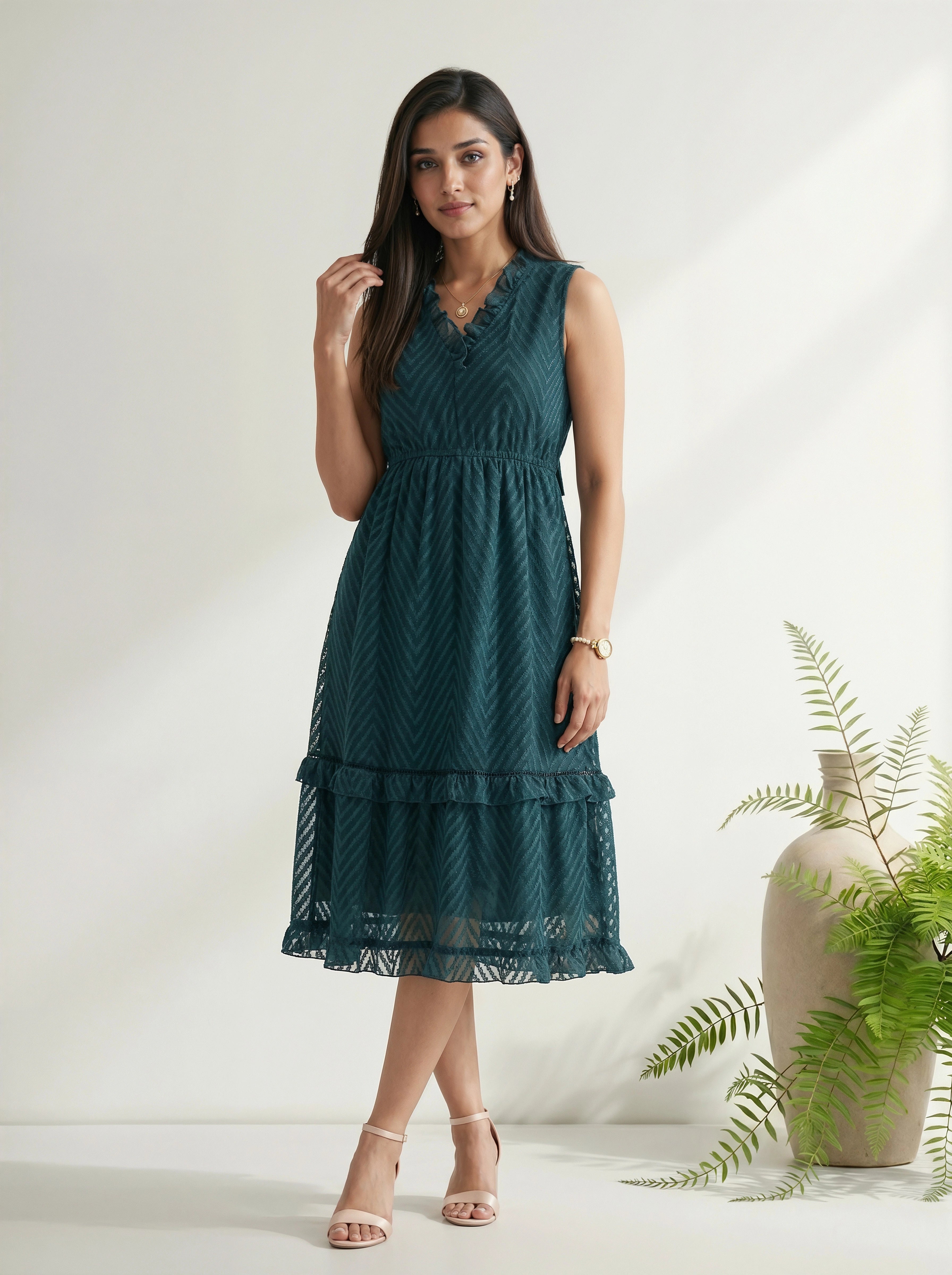Woman wearing a teal dress standing against a white background with a plant to the side.