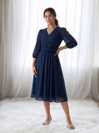 Woman wearing a navy blue dress standing in front of white curtains.