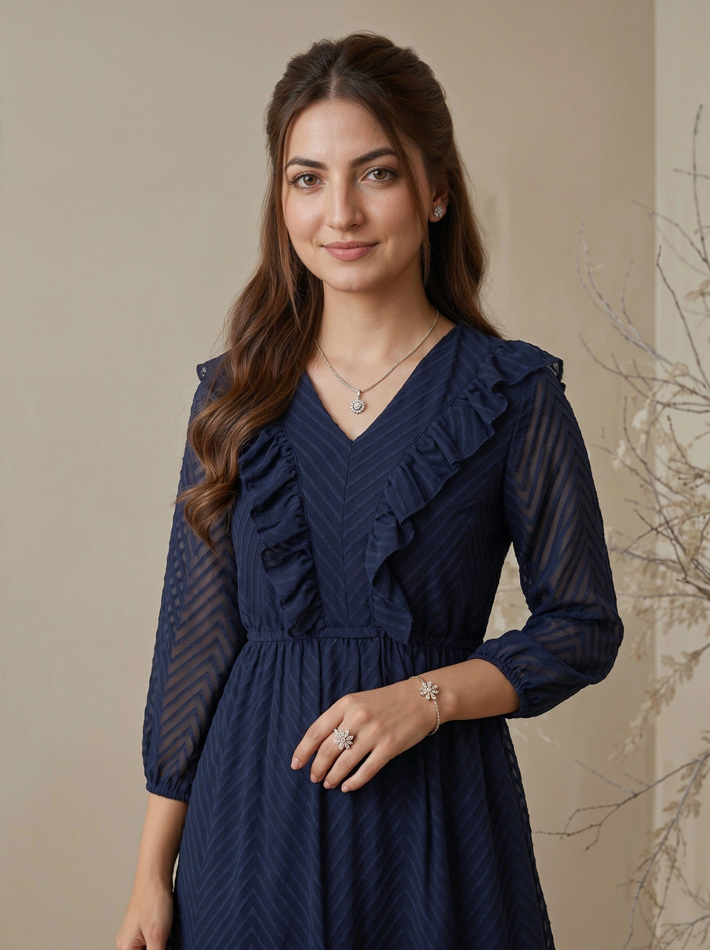 Woman wearing a navy blue dress with ruffled details against a beige wall.