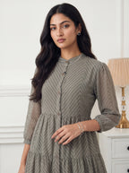 Woman wearing a gray patterned dress in a room with a lamp and white wall.