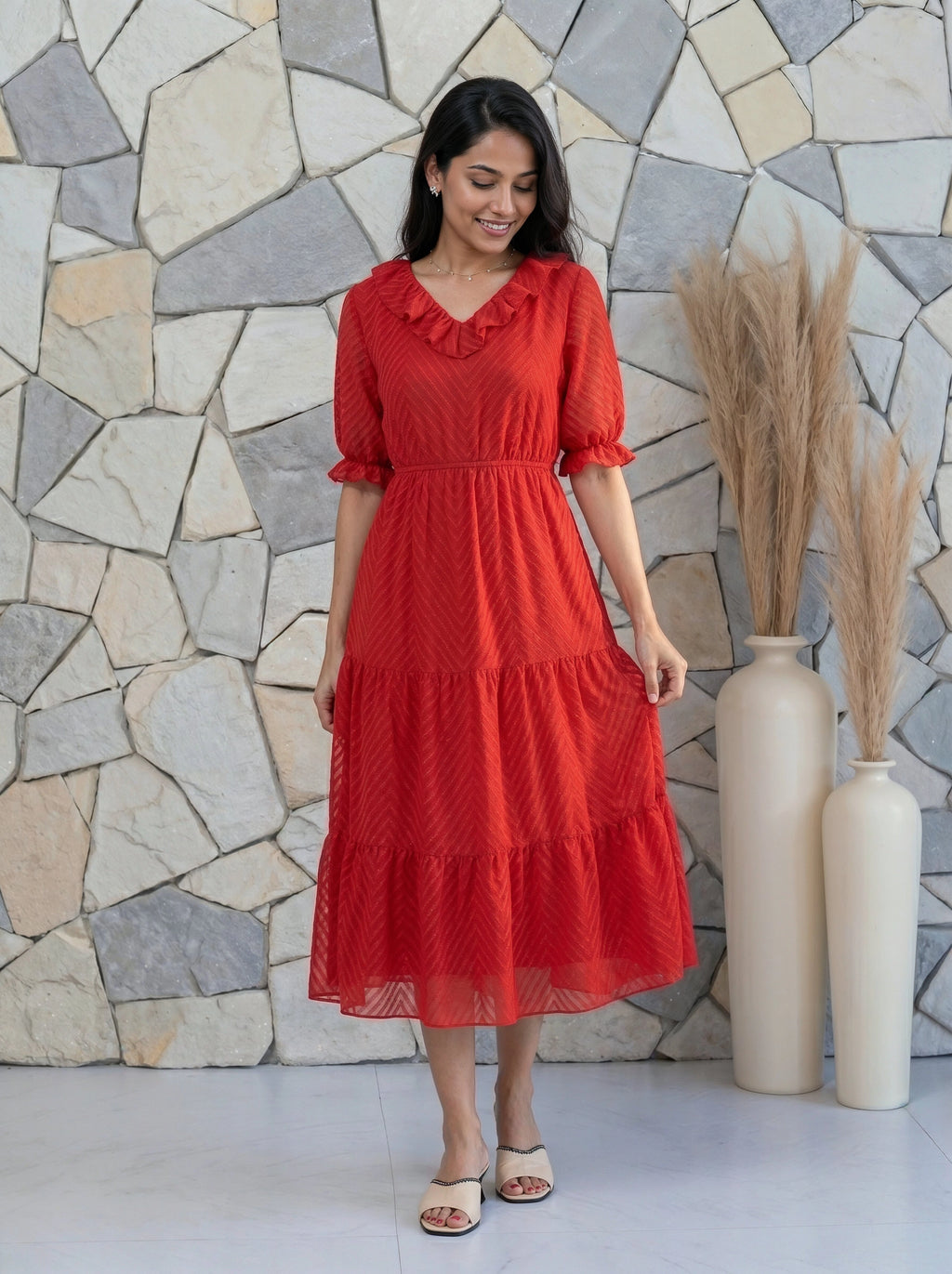 Woman in a red dress standing against a stone wall with decorative vases.