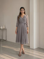 Woman wearing a gray patterned dress standing in a minimalistic room.