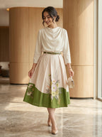 Woman wearing a white and green dress with floral patterns in an indoor setting.