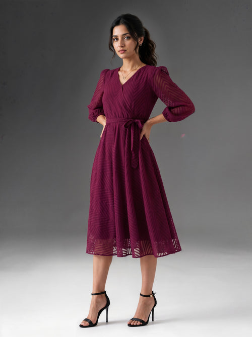 Woman wearing a burgundy dress with long sleeves against a gray background