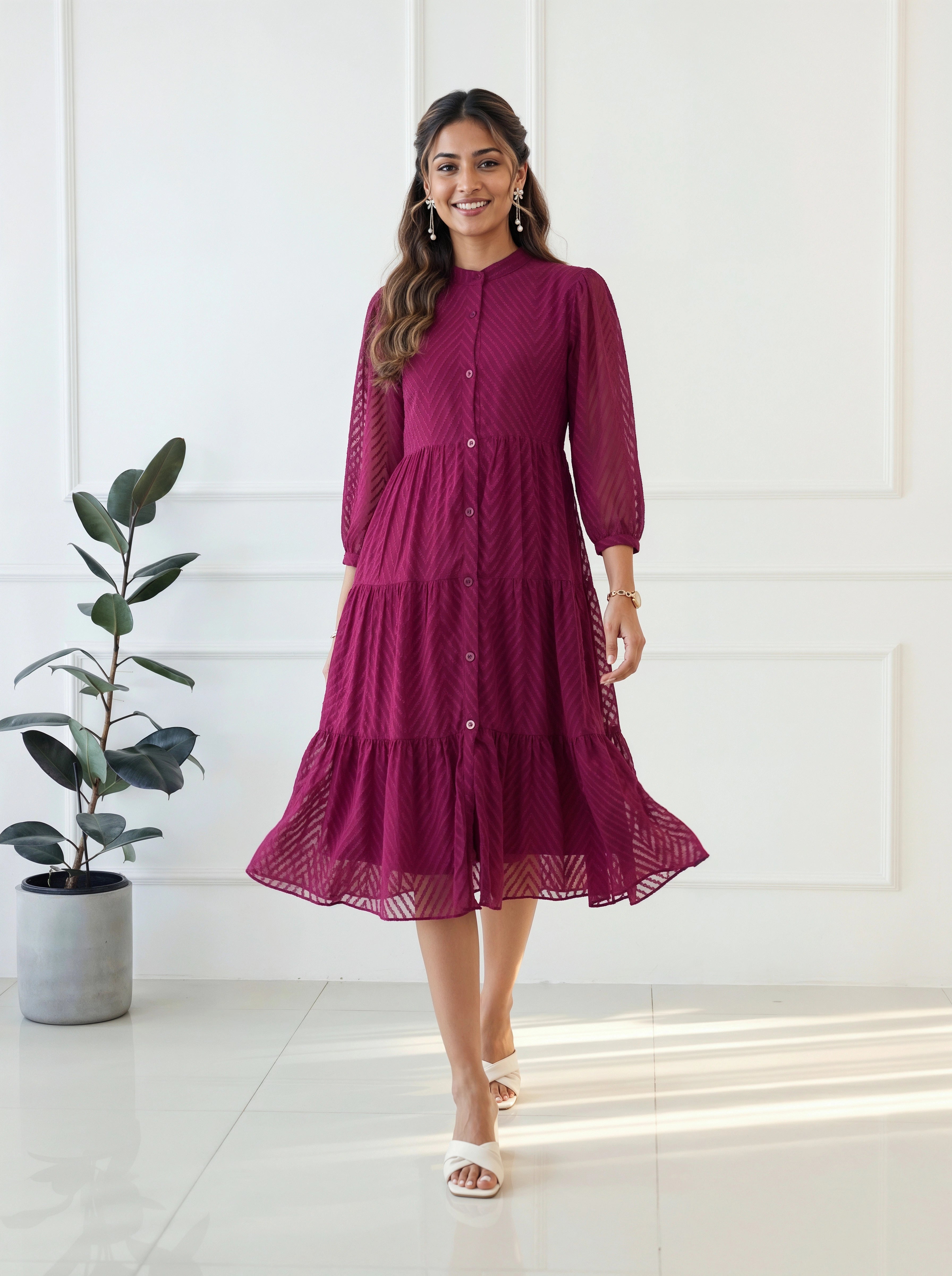 Woman wearing a burgundy dress standing in a bright room with a plant.