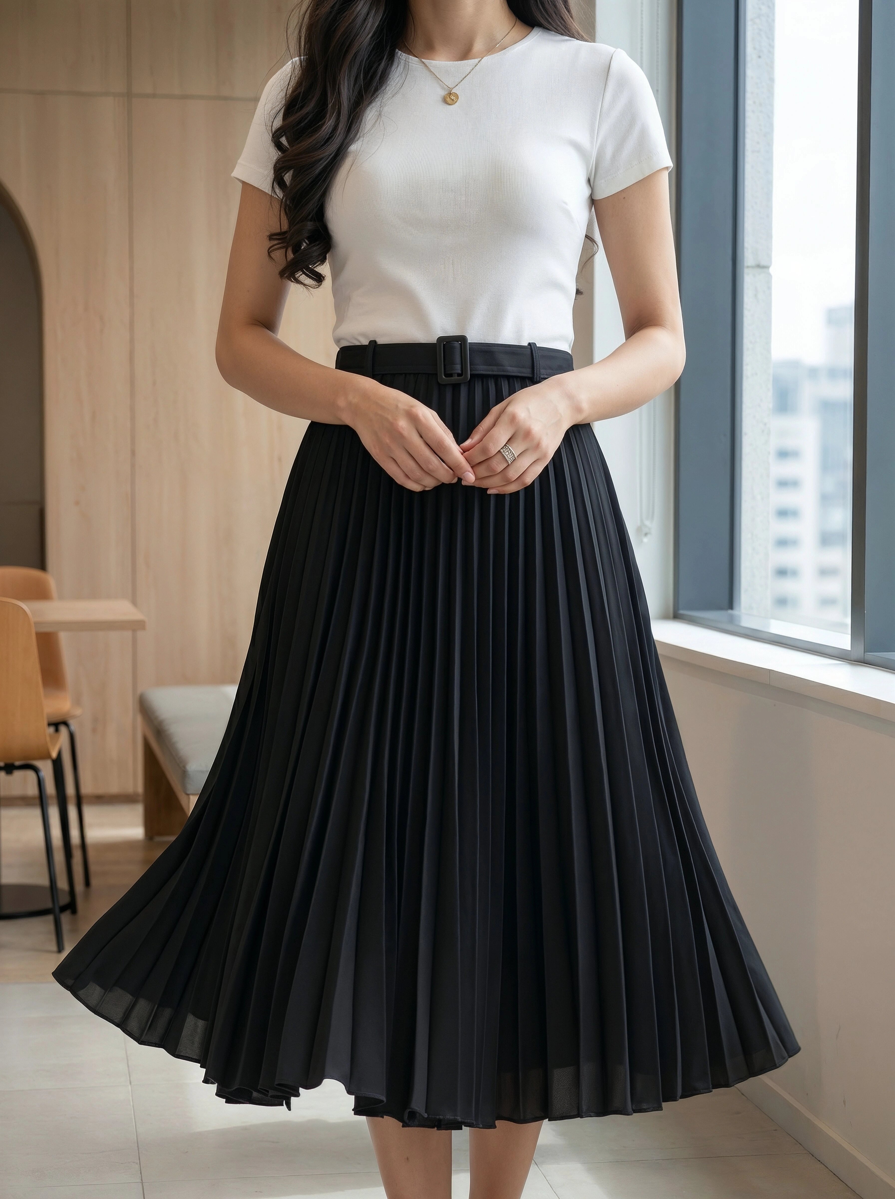 Woman wearing a white top and black pleated skirt in an indoor setting.