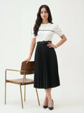 Woman wearing a white top and black pleated skirt standing next to a chair on a white background