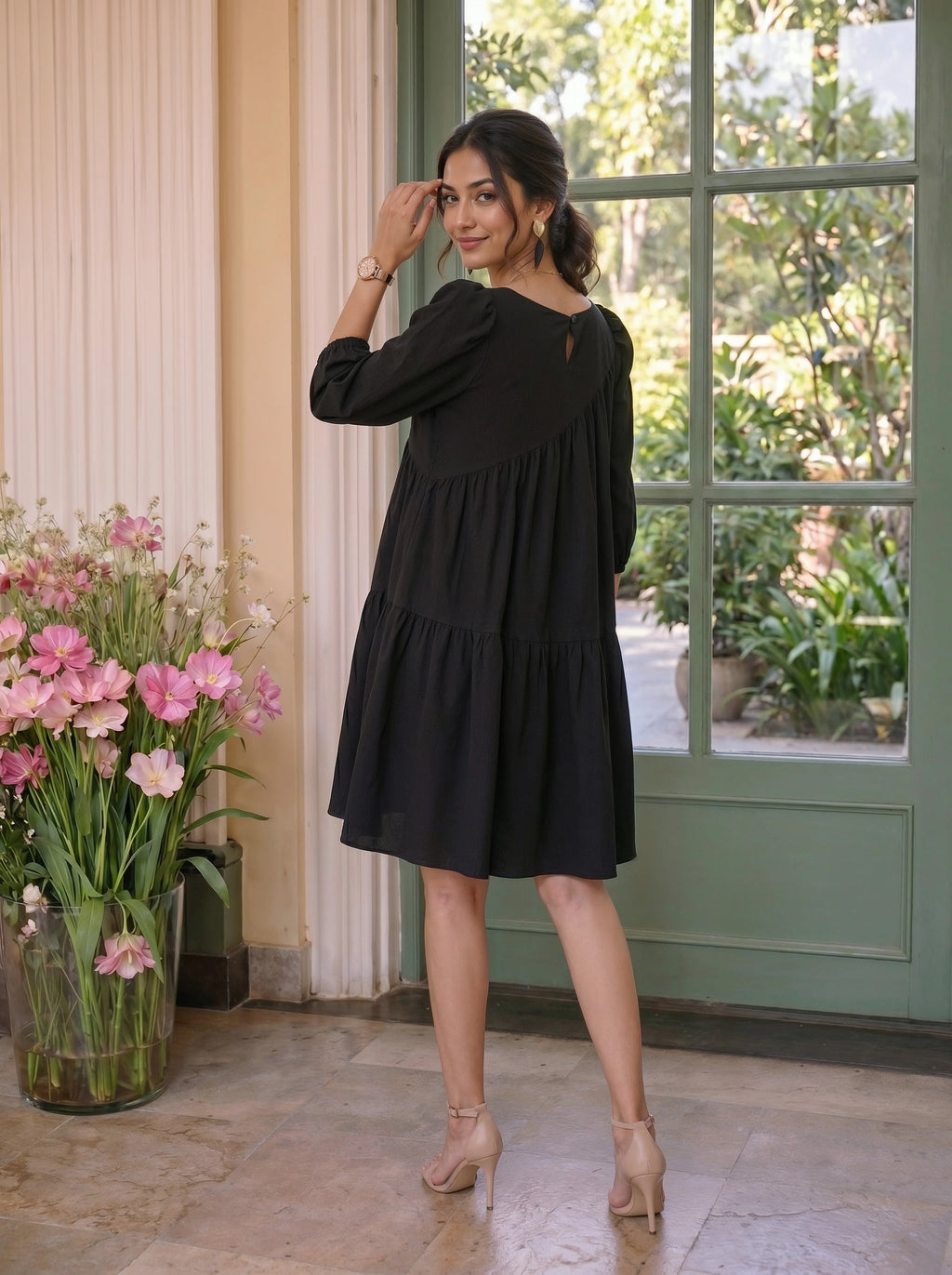 Woman in a black dress standing in a room with flowers and a green door.