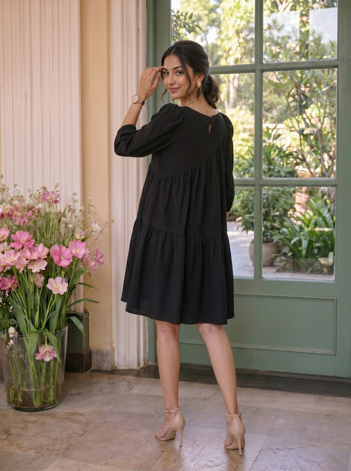Woman in a black dress standing in a room with flowers and a green door.