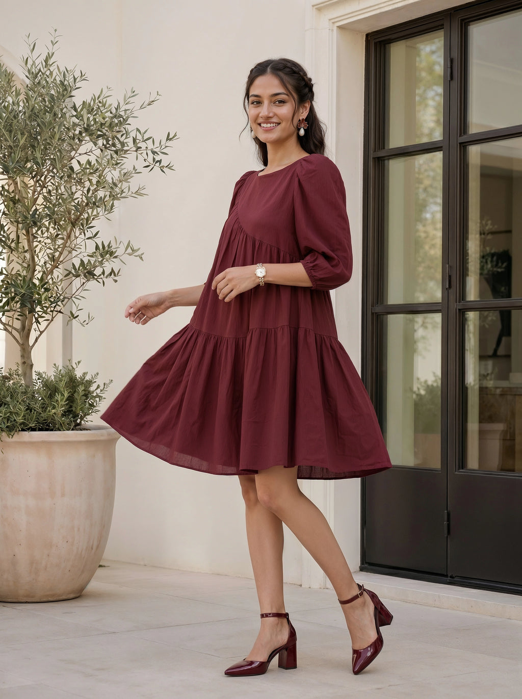Woman in a burgundy dress standing outdoors next to a building with large windows.