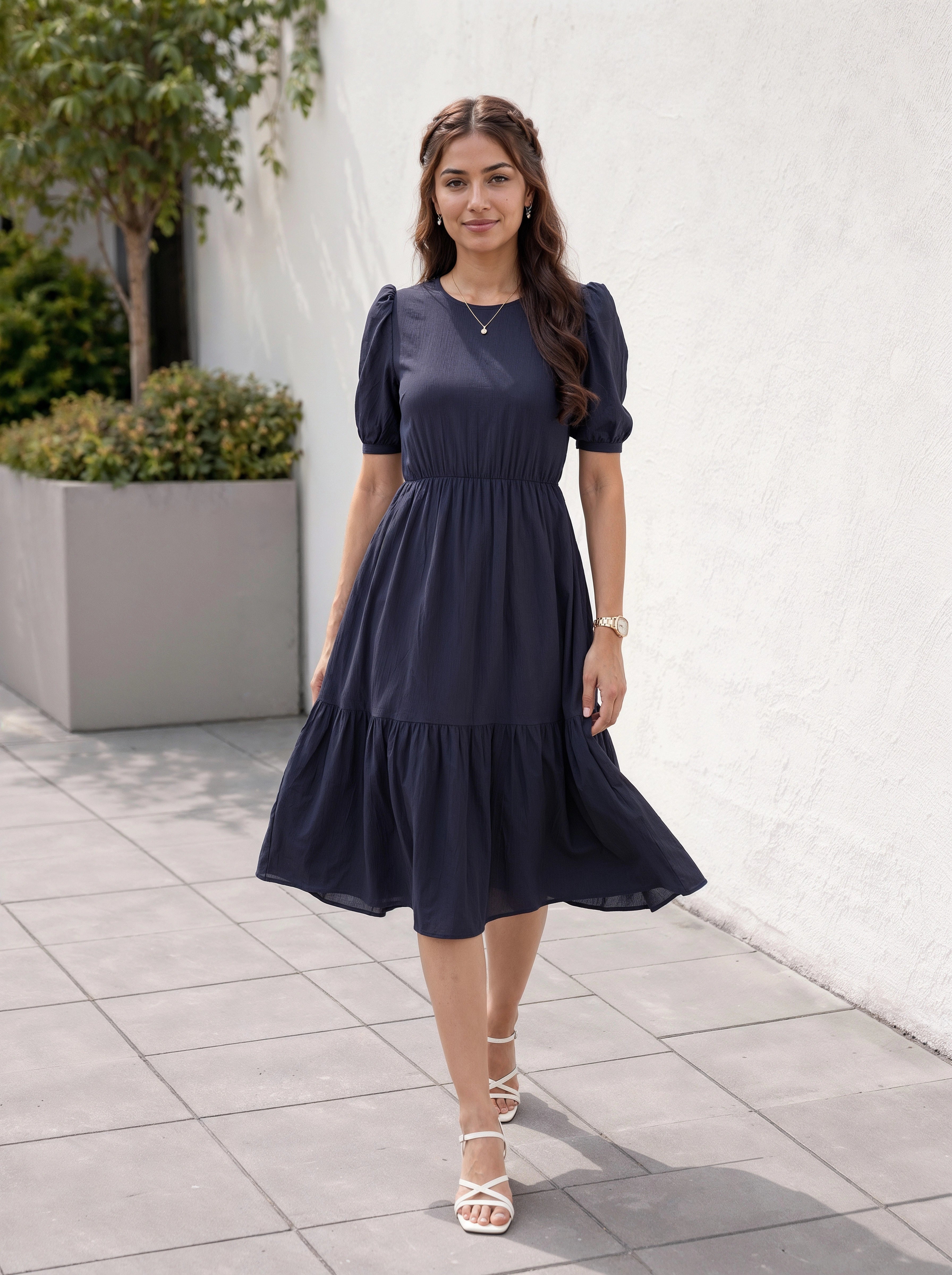 Woman wearing a navy blue dress standing outdoors on a tiled floor.