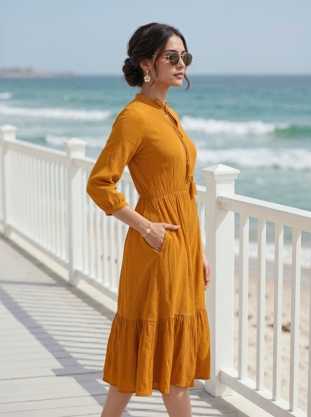 Woman in a yellow dress standing on a wooden deck by the ocean.