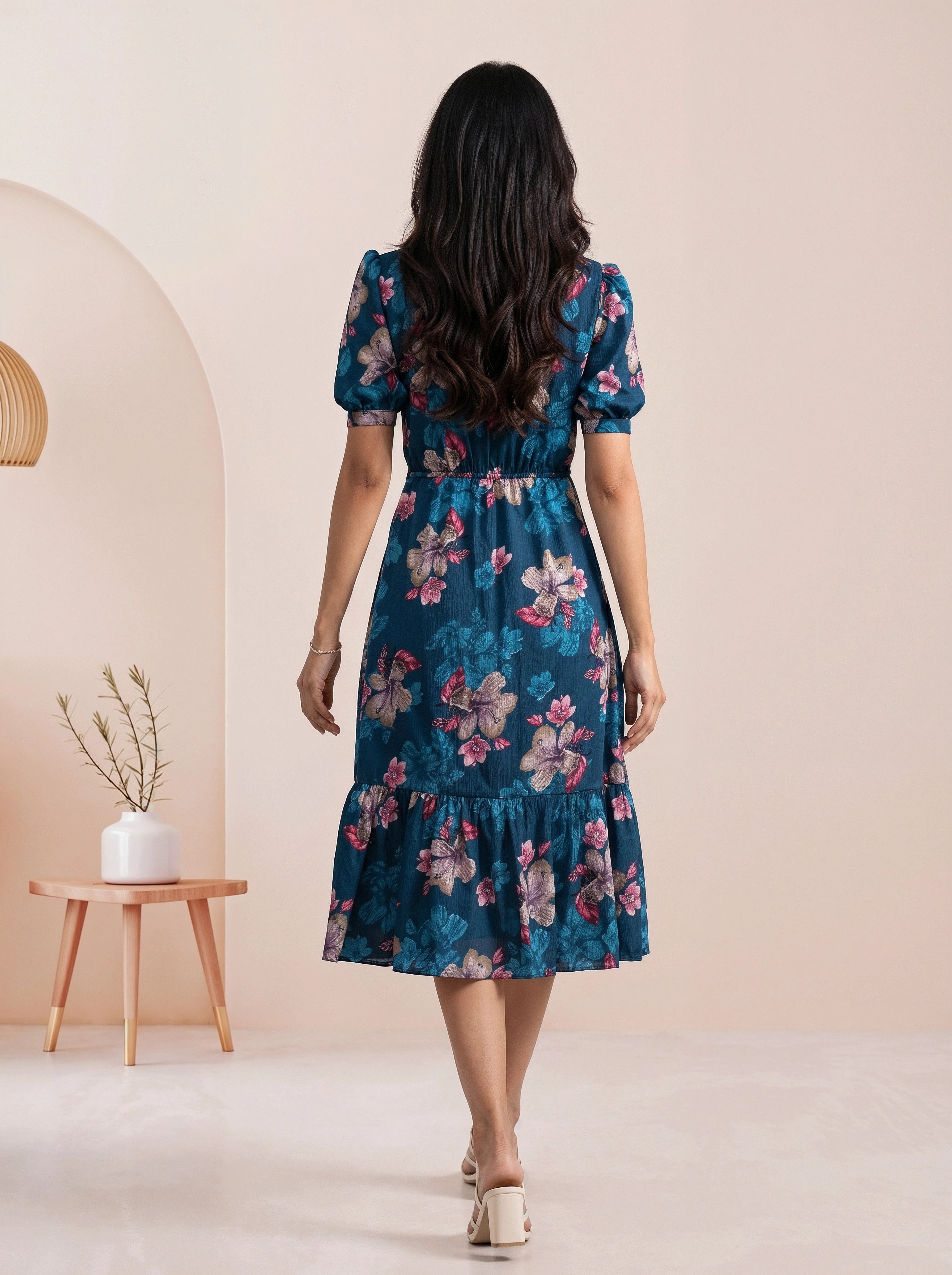 A woman models a navy blue midi dress with a matching sheer open-front cardigan featuring a geometric pattern, set against a warm beige backdrop with draped cream fabric.