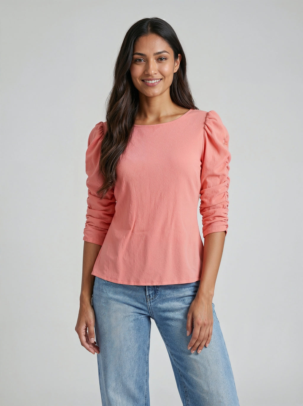 Woman wearing a pink top with puffed sleeves and blue jeans on a gray background